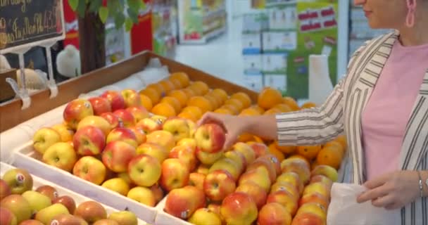 Mädchen wählt Produkte, Gemüse, Obst im Laden. Hübsche junge schöne Frau kauft Lebensmittel, Obst, Äpfel, Tomaten, Orangen auf dem Markt, im Supermarkt. Einkaufen, vegane Verkäufe — Stockvideo