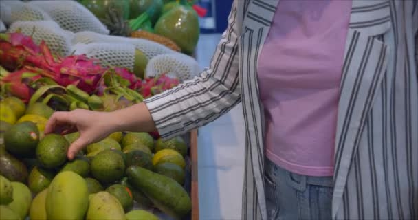 Eine junge Frau in der Lebensmittelabteilung eines Supermarktes kauft Lebensmittel ein, wo die Leute Lebensmittel kaufen. Hübsche Frau kauft Lebensmittel, Obst, Äpfel, Orangen auf dem Markt, im Supermarkt.