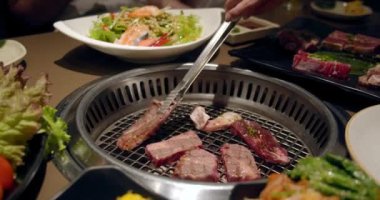 Şef tong 'u kullanıyor ve eti ızgaraya çeviriyor. Ateş yanıyor, yağlı biftek yavaş çekimde pişiyor. Izgara, lezzetli biftek yavaş çekimde yakın çekim..