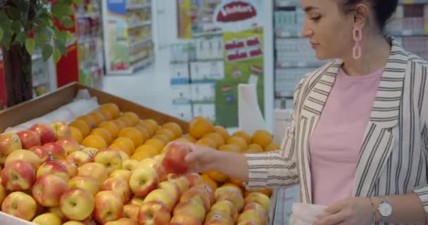 Mooie jonge mooie vrouw koopt eten, fruit, appels, tomaten, sinaasappels op de markt, in de supermarkt. Winkelen, Vegan verkoop concep — Stockvideo