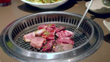 Izgara, lezzetli biftek yavaş çekimde yakın çekim. Şef tong 'u kullanıyor ve eti ızgaraya çeviriyor. Ateş yanıyor, yağlı biftek yavaş çekimde pişiyor..