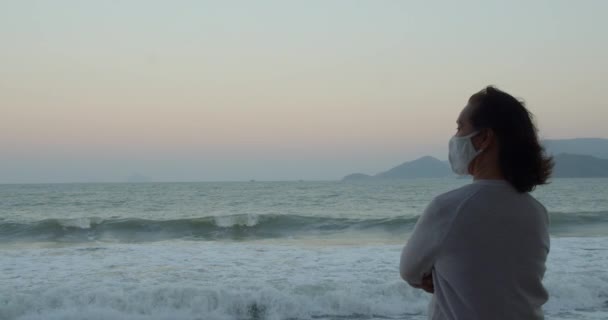 Een oudere vrouw met een beschermend masker doet oefeningen en geniet van het uitzicht op zee met een covid-19 masker op. Gezondheids- en veiligheidsconcept, coronavirus, virusbescherming, pandemie. — Stockvideo