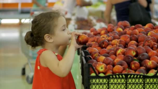 Ребенок выбирает продукты. Ребенок красивая девушка с вьющимися волосами, покупает еду с родителями в супермаркете, выбирает вкусные фрукты, персики, яблоки, апельсины на рынке, в супермаркете. — стоковое видео