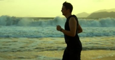 Genç beyaz bir adamın silueti arka planda egzersiz yapıyor. Güzel bir deniz manzarası. Gün batımında kumsalda koşuyor.