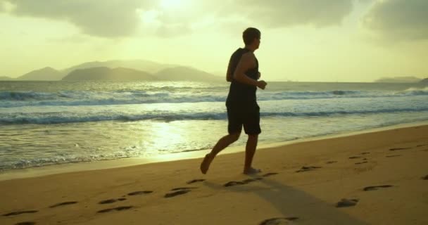Бег трусцой по песку на пляже на закате на фоне прекрасного моря, больших красивых волн. Бегун, здоровый образ жизни. Триатлон бег, тренировки на выносливость, спринт. — стоковое видео