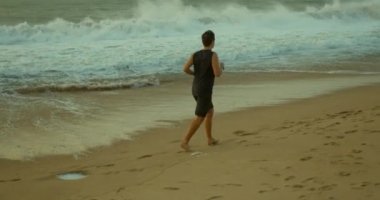 Genç beyaz adam güzel bir deniz altyapısı olan açık havada koşuyor. Gün batımında kumsalda koşmak güzel denizin arka planına karşı, büyük güzel dalgalar..