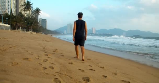 Giovane uomo caucasico che cammina sulla sabbia lungo la riva all'aperto sullo sfondo del bellissimo mare.Walk sulla sabbia sulla spiaggia al tramonto sullo sfondo del mare — Video Stock