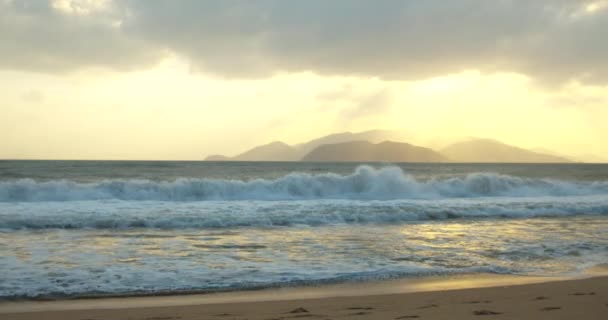 Fondo de playa asiática. El rastro del sol en las olas en la arena. Gran sol aparece detrás de las nubes, y grandes montañas tocan el horizonte y la costa. — Vídeos de Stock