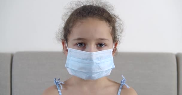 Retrato bonito criança pequena ou menina em uma máscara médica protetora, com um rosto triste desapontado. Uma rapariga com uma máscara médica. Pandemia, covid - 19. — Vídeo de Stock