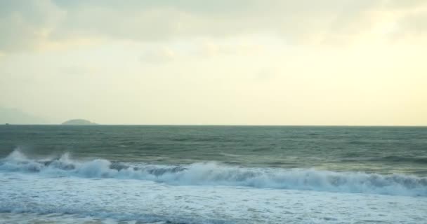 Un gran sol aparece detrás de las nubes, y grandes montañas tocan el horizonte y la costa. Fondo de playa asiática. El rastro del sol en las olas en la arena. — Vídeo de stock