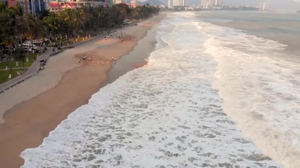 La gente juega al fútbol en la playa de la ciudad y hermosas olas de olas marinas chocan en la orilla arenosa. 4K — Vídeo de stock