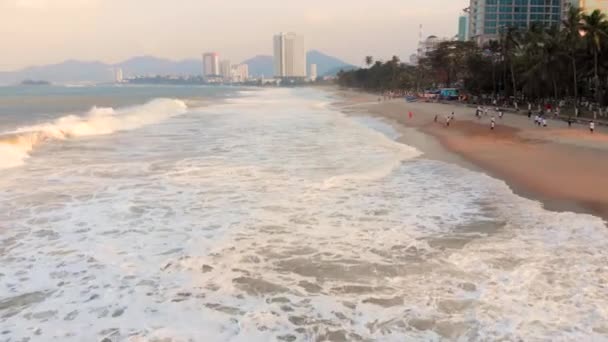 Σκοποβολή από ένα drone εναέρια με φόντο ένα πορτοκαλί ηλιοβασίλεμα με θέα τα κύματα της θάλασσας του ωκεανού, την παραλία της πόλης και τα όμορφα κύμματα των κυμάτων της θάλασσας συντριβή κατά την αμμώδη ακτή. 4K — Αρχείο Βίντεο