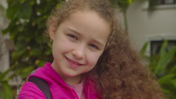 Portrét Legrační holčička usmívající se dítě dívající se do kamery se procházejí po ulici, roztomilé dítě s pěknou tváří na ulici. Koncept šťastného dětství. — Stock video