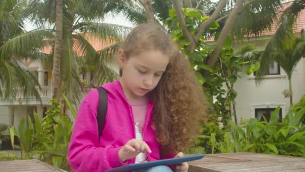 Schattig klein meisje kind met behulp van een digitale tablet technologie apparaat telefoon of laptop.Speelt in de telefoon zit op straat alleen.Kinderen tech verslaving concept spel spelen. — Stockvideo