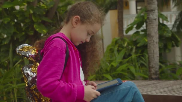 Plays in the phone sitting on street alone.Children tech addiction concept play game. Cute little girl child using a digital tablet technology device telephone or laptop. — Stock Video