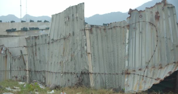 Κοντινό πλάνο - ένας παλιός φράχτης φτιαγμένος από φύλλα κασσιτέρου και κρυπτογραφημένα φύλλα, κολόνες, τυλιγμένος σε σκουριασμένο συρματόπλεγμα, στο τέλος της ημέρας, και υπάρχουν πολλά σκουπίδια κοντά. — Αρχείο Βίντεο