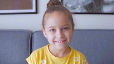 Portre Komik küçük kız kameraya bakıyor evde kanepede oturuyor, güzel yüzlü şirin çocuk kanepede oturuyor. Mutlu bir çocukluk kavramı.