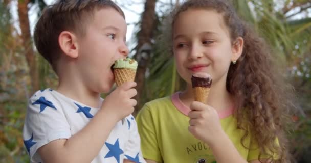 Portret wesoły dzieci uśmiechnięte dzieci szczęśliwy chłopiec i dziewczynka jedząc lody i zabawy patrząc na siebie. — Wideo stockowe