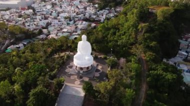 Vietnam 'daki dev Buda heykelinin etrafında uçan hava manzarası yeşil palmiyelerin, ağaçların ve kentsel altyapıların konut barakalarının zeminine karşıdır.