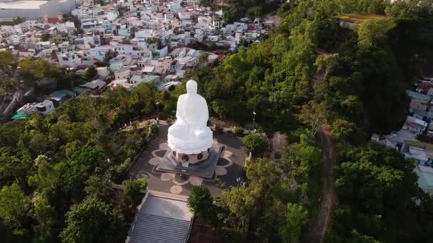 Légi kilátás repül körül a hatalmas Nagy Buddha szobor Vietnamban, hátterében a zöld tenyér vagy fák és lakótelepi laktanyák városi infrastruktúra.Fehér Nagy Buddha az egyik attrakció — Stock videók