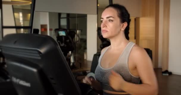 Jeune Indienne travaillant sur un tapis roulant dans une salle de fitness. Gros plan d'une sportive vêtue de leggings gris et d'un haut, courant sur un tapis roulant, faisant du sport. — Video