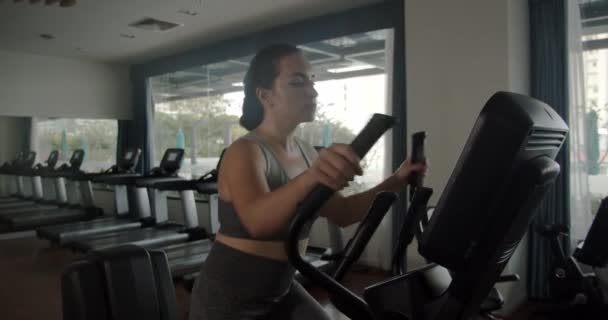 Mujer india joven haciendo ejercicio en una cinta de correr en una sala de fitness. Primer plano de una chica deportiva vestida con polainas grises y una parte superior, corriendo en una cinta de correr, entrando a hacer deporte. — Vídeo de stock