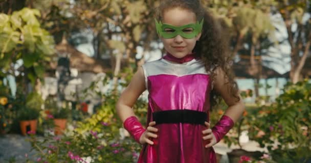 Menina bonita no traje de super-herói, criança joga super-herói, criança vestida com um manto rosa e a máscara do herói. Super-herói e conceito de poder. Retrato de perto. — Vídeo de Stock