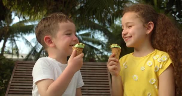 Portret vrolijke kinderen glimlachende kinderen gelukkig baby jongen en klein meisje eten ijs en plezier hebben kijken naar elkaar. — Stockvideo