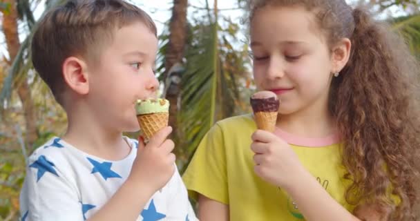 Copii zâmbitori Băiețel fericit și fată care mănâncă înghețată și se distrează uitându-se unul la celălalt . — Videoclip de stoc