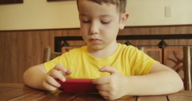Telefona bakan, masada oturan bir çocuğun portresi. Anaokulu öğrencisi akıllı telefonda yapay zeka kullanıyor. Bebek telefonda video izliyor..