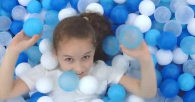 Neşeli küçük bir kızın portresi, gülümseyen bir çocuk, plastik toplardan fırlıyor, çocuk kameraya bakıyor, güzel yüzlü güzel bir kız çocuğu, seviniyor. Mutlu çocukluk kavramı