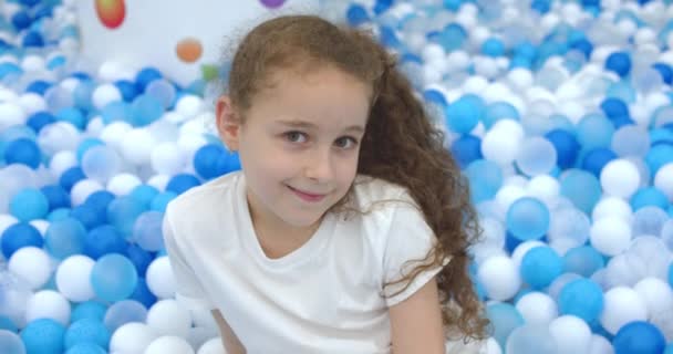 Ritratto di una bambina allegra, bambino sorridente, su palle di plastica per bambini di sfondo, bambino guarda la macchina fotografica, una bambina carina con un bel gioco di faccia a casa, gioisce. Buona infanzia. — Video Stock