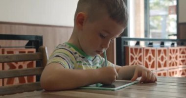 Bir çocuk portresi evdeki bir masaya oturur ve tabletine özel bir kalemle resim çizer. Anaokulu öğrencisi resim yapmak için özel bir tablet kullanır..