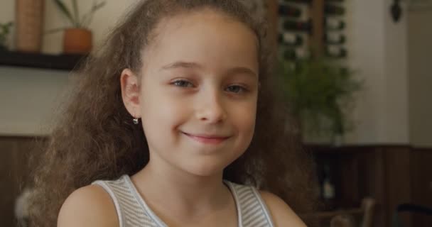 Portrait of funny little girl, smiling child, looking at camera, sitting at the table at home, cute kid child with pretty face. Happy childhood concept. — Stock Video