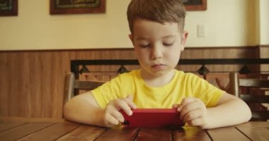 Telefona bakan, masada oturan bir çocuğun portresi. Anaokulu öğrencisi akıllı telefonda yapay zeka kullanıyor. Bebek telefonda video izliyor..