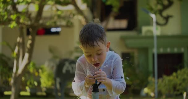 Симпатичный счастливый ребенок, играющий с садовым распылителем в жаркий летний день. Малыш веселится на заднем дворе прыгая под брызгающей водой из шланга. Мальчик счастливого детства. — стоковое видео