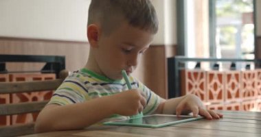 Bir çocuk portresi evdeki bir masaya oturur ve tabletine özel bir kalemle resim çizer. Anaokulu öğrencisi resim yapmak için özel bir tablet kullanır..