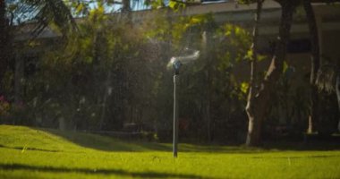 Yeşil bir parkta çalışan tam otomatik sulama sistemiyle aktif hale getirildi. Yeşil çimenleri sulayan fıskiyeler. 4K Ham Görüntü.