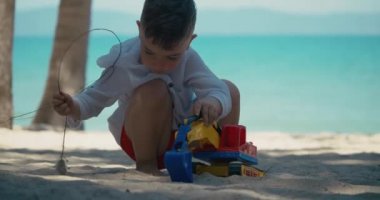 Çocuk plajdaki kumda plastik bir arabayla oynuyor. Sahilde kumla oynayan çocukların elleri, plastik oyuncaklar..