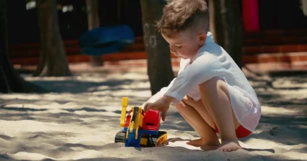 L'enfant joue avec une voiture en plastique dans le sable sur la plage. gros plan des mains des enfants jouant avec le sable sur la plage, jouets en plastique. — Video