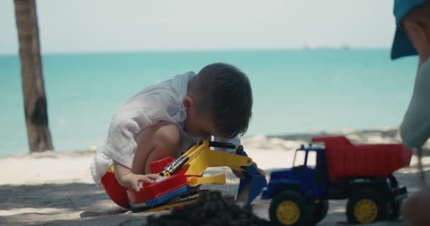 Los niños juegan con un coche de plástico en la arena de la playa. primer plano de los niños manos jugando con arena en la playa, juguetes de plástico. — Vídeo de stock