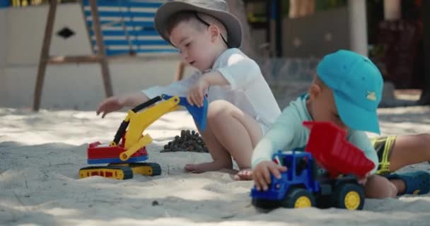Los niños juegan con una grúa de plástico y un coche en la arena de la playa. primer plano retratos de niños y niños manos jugando con arena en la playa, juguetes de plástico. — Vídeo de stock