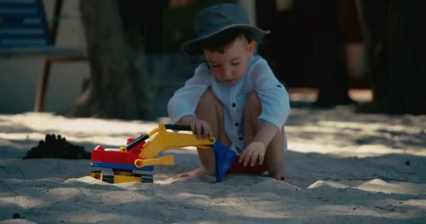 Niño juega con un coche de plástico en la arena en la playa. primer plano de los niños manos jugando con arena en la playa, juguetes de plástico. — Vídeos de Stock