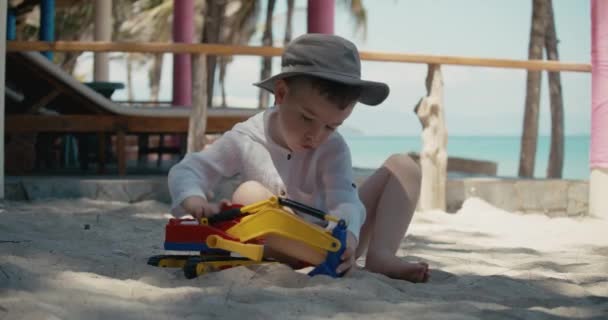 Niño juega con un coche de plástico en la arena en la playa. primer plano de los niños manos jugando con arena en la playa, juguetes de plástico. — Vídeos de Stock