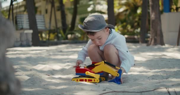 Lindo niño jugar con una grúa de plástico y un coche en la arena en la playa. Primer plano retratos de niños y niños manos jugando con arena en la playa, juguetes de plástico. — Vídeo de stock