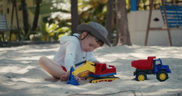 Los niños juegan con un coche de plástico en la arena de la playa. primer plano de los niños manos jugando con arena en la playa, juguetes de plástico. — Vídeo de stock