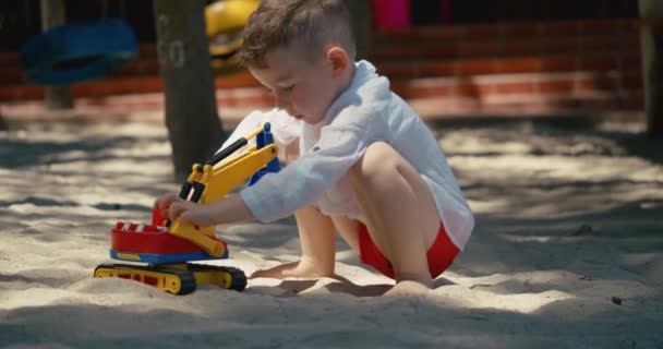 L'enfant joue avec une voiture en plastique dans le sable sur la plage. gros plan des mains des enfants jouant avec le sable sur la plage, jouets en plastique. — Video