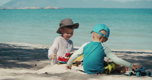 子供たちはビーチでプラスチック製のクレーンと砂の上の車で遊んでいます。ビーチで砂と遊ぶ子供や子供たちの手のクローズアップ肖像画、プラスチック製のおもちゃ. — ストック動画