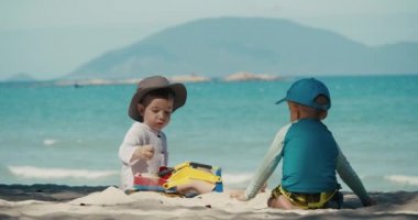 Çocuklar plajda plastik bir vinç ve kumsalda bir arabayla oynuyorlar. Sahilde kumla oynayan çocukların ve çocukların yakın plan portreleri, plastik oyuncaklar..