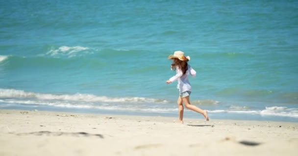 帽子の面白い女の子は、ビーチに沿って海岸に沿って実行され、海によって晴れた日に子供、幸せ、海によってビーチで子供。幸せな子供時代のコンセプト. — ストック動画